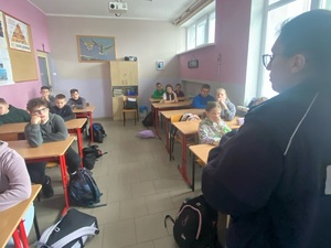 Uczniowie siedzący w ławkach i policjantka w roli prelegenta.