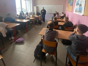 Uczniowie siedzący w ławkach i policjantka w roli prelegenta.