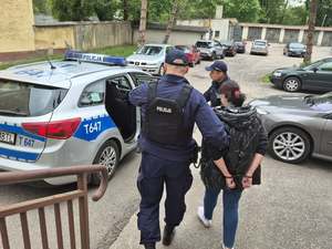 Policjanci prowadzą zatrzymaną do radiowozu.