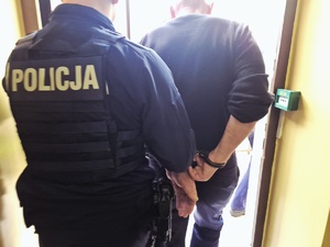 policjant prowadzi zatrzymanego mężczyznę z kajdankami na rękach