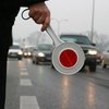 policjant trzymający białą tarczę do zatrzymywania pojazdów na tle ruchliwej drogi